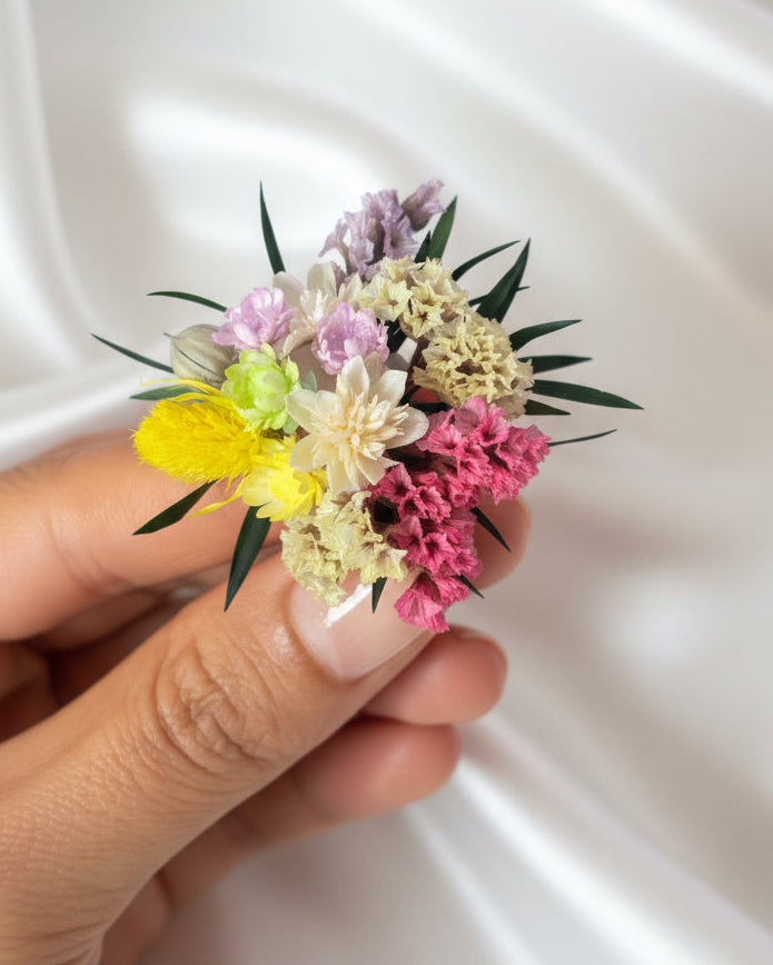 Hand holding a small bouquet of colorful flowers against a white satin background
