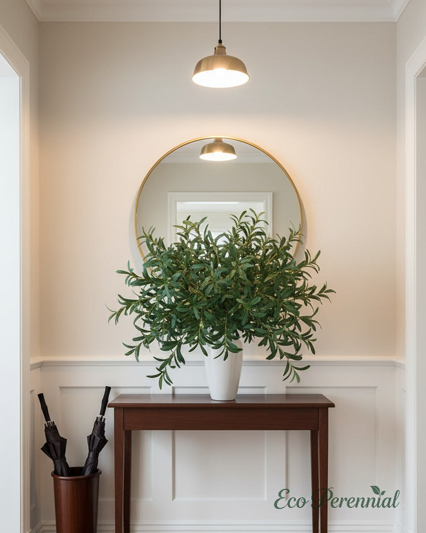 Eco Perennial artificial olive branches with elegant green-grey leaves in a tall navy blue ceramic vase on a slim entryway console table against light grey walls with gold-framed mirror