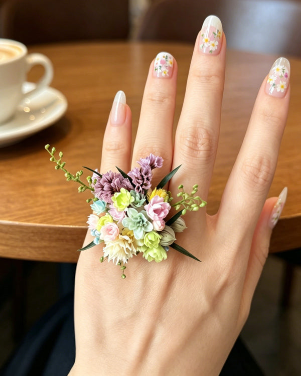 Hand wearing a floral ring with a blurred coffee cup in the background