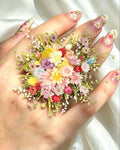 Hand with floral nail art holding a small bouquet of flowers against a white background