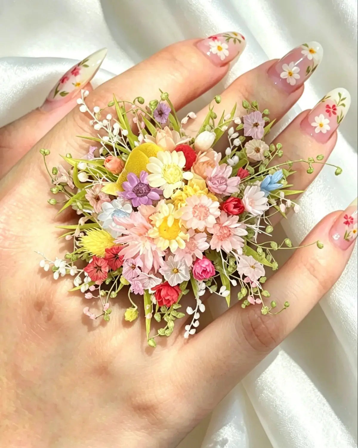Hand with floral nail art holding a small bouquet of flowers against a white background